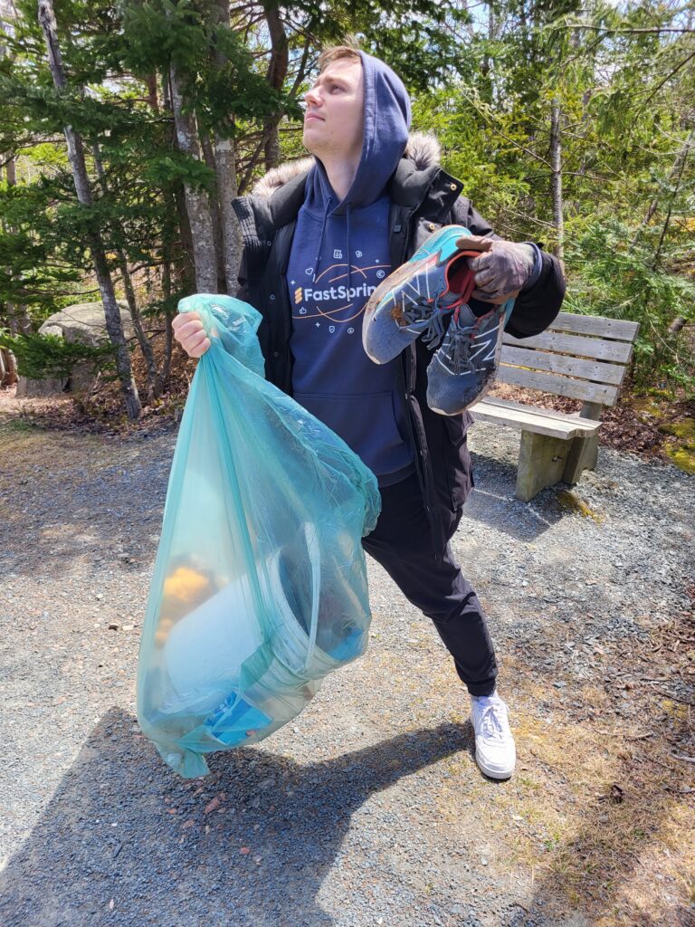 A man holds a bag of trash and a pair of shoes he picked up while cleaning up a park.