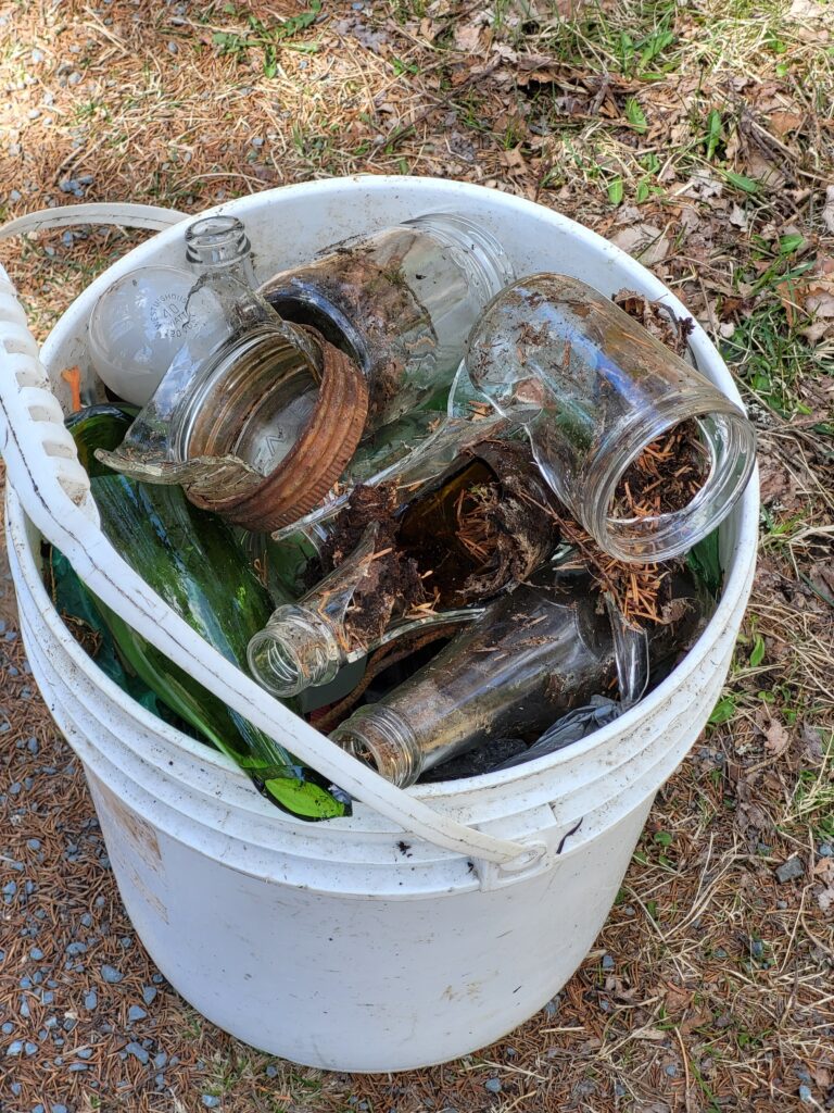 A bucket full of collected trash and broken glass bottles.
