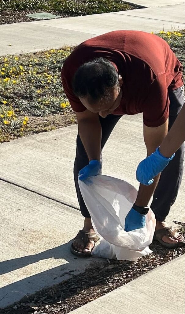 A man is bending over to put trash into a trash bag.