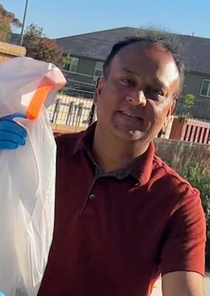 A close up image of a man smiling at the camera while holding up a bag of trash.