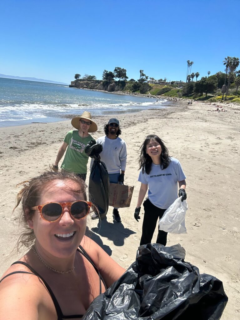 Four people smile at the camera while holding trash bags on a beach.