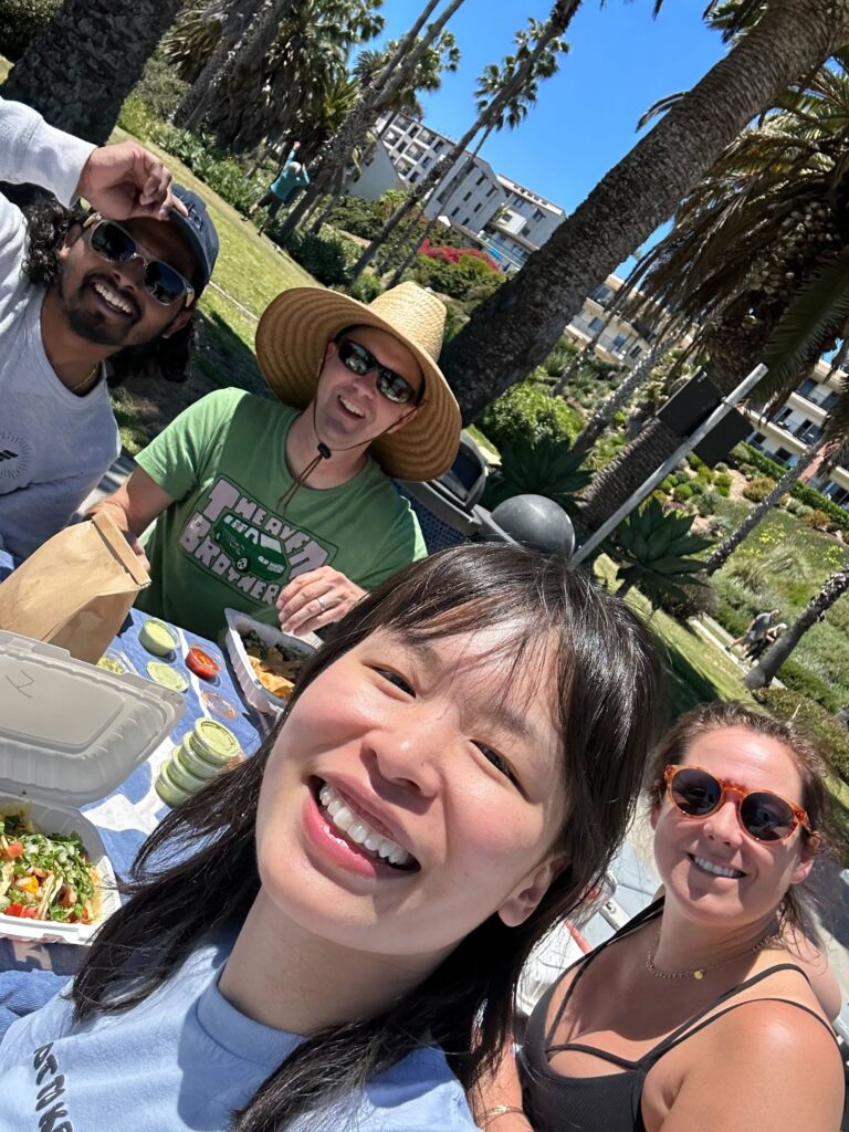 Four people having a picnic with palm trees and buildings behind them.