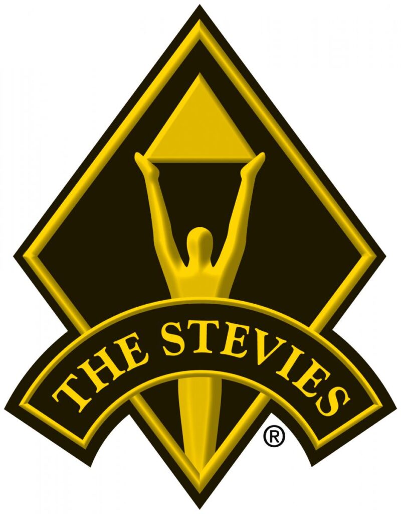 A black and gold logo of a humanoid shape with its hands above its head holding a pyramid, with text spelling The Stevies in the foreground.