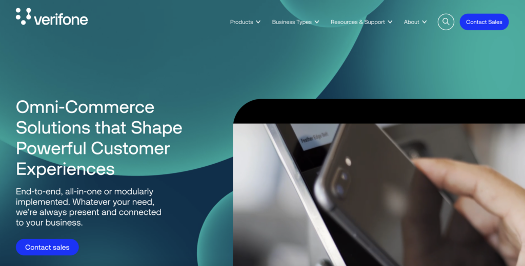 Screenshot of international payment gateway Verifone's homepage, teal with white text and a close-up photo of a hand holding a phone to a point of sale device.