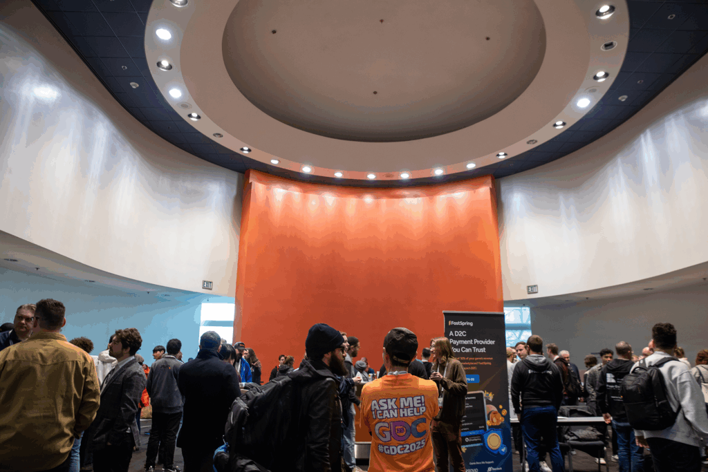 The busy hall for the FastSpring happy hour had an orange backdrop and round recessed ceiling.
