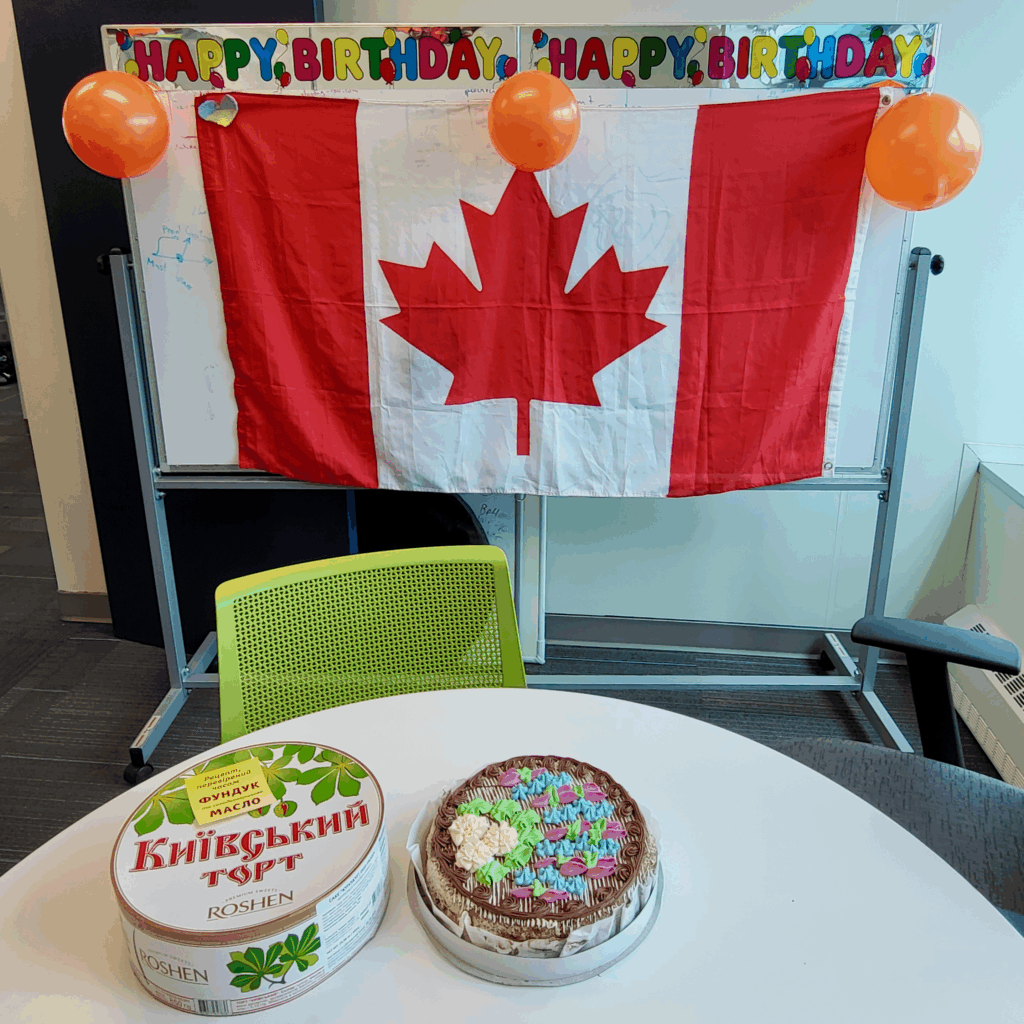 A Canadian flag hanging behind a small office table that holds a Kyiv cake and its box.