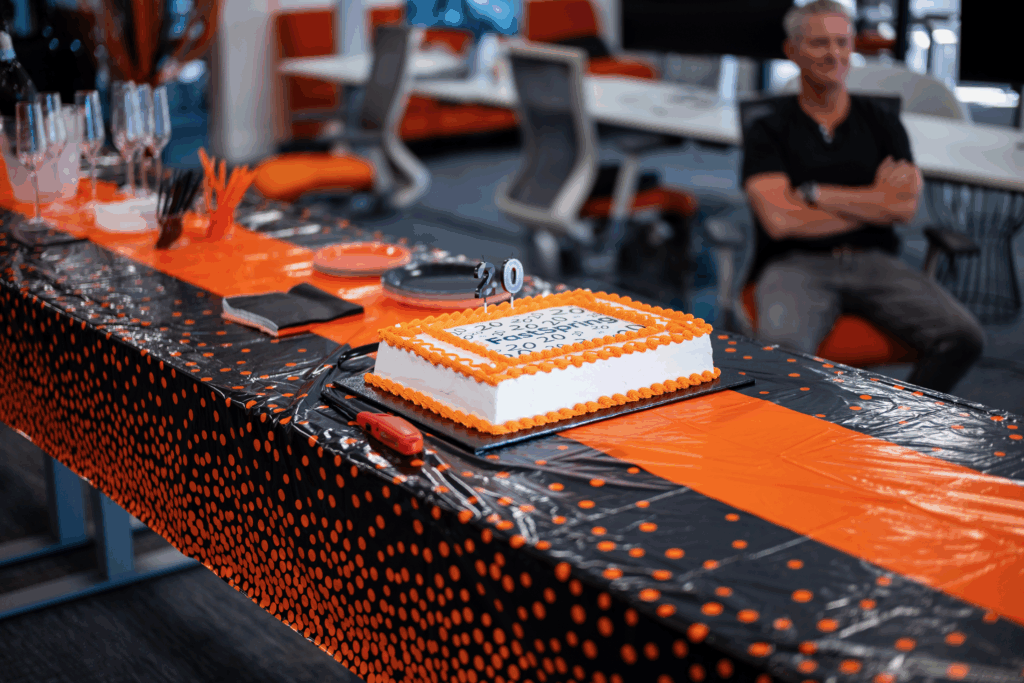 An orange and white cake on a long table with a black and orange tablecloth.