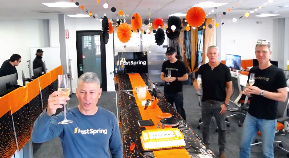 FastSpring CEO David Nachman in the foreground raising a toast to FastSpring's 20 years, with 3 more employees standing behind to the right beside the cake table.