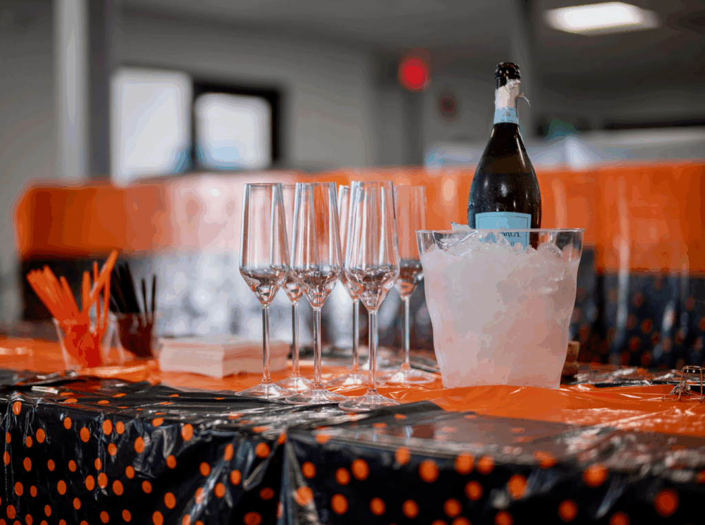 Champagne glasses and a bottle of champagne on an orange and black table with an orange and black backdrop.