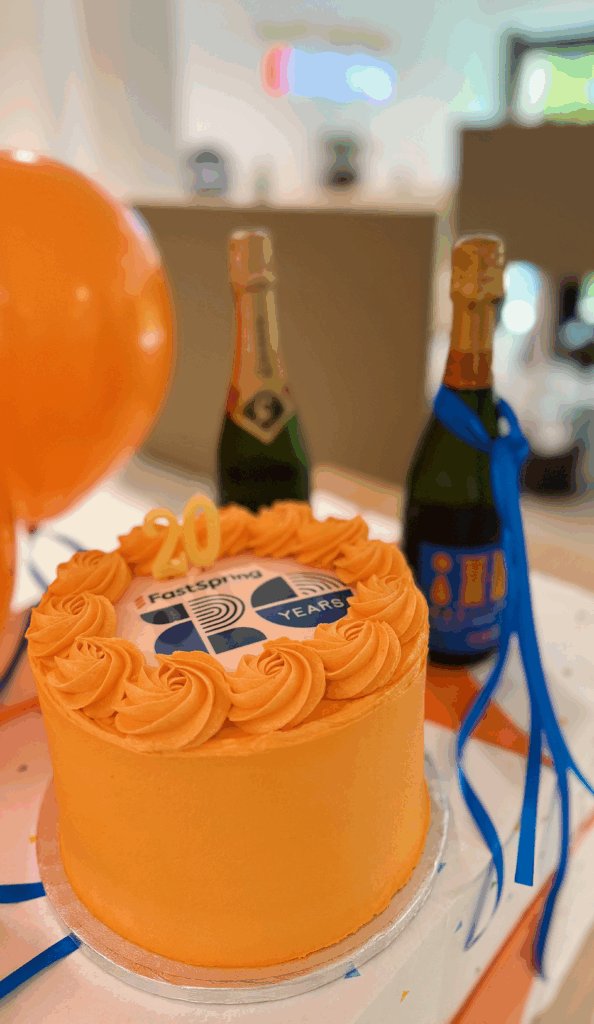 An orange cake with the FastSpring 20 years logo, beside two bottles of champagne.