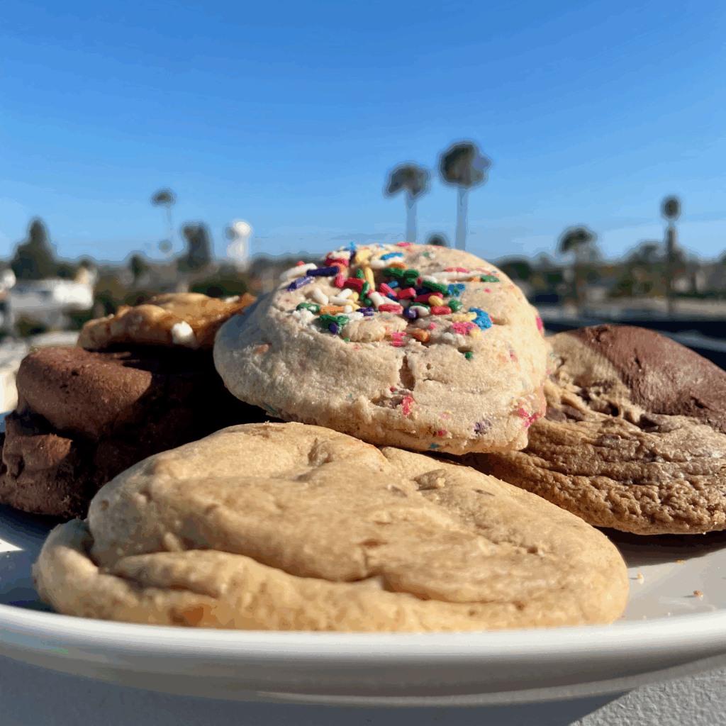 A plate of gourmet drop cookies in front of an out-of-focus background of palm trees and a blue sky.