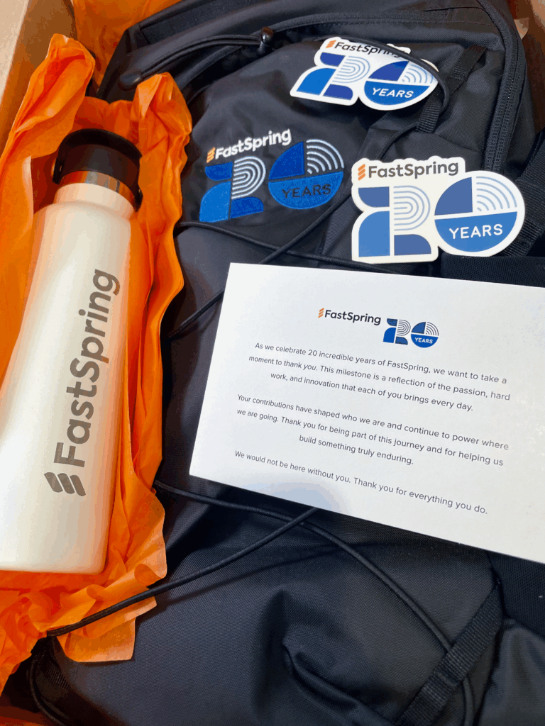 A white bottle wrapped in orange paper, a black backpack with blue logo and stickers, and an enclosed note from FastSpring to employees.