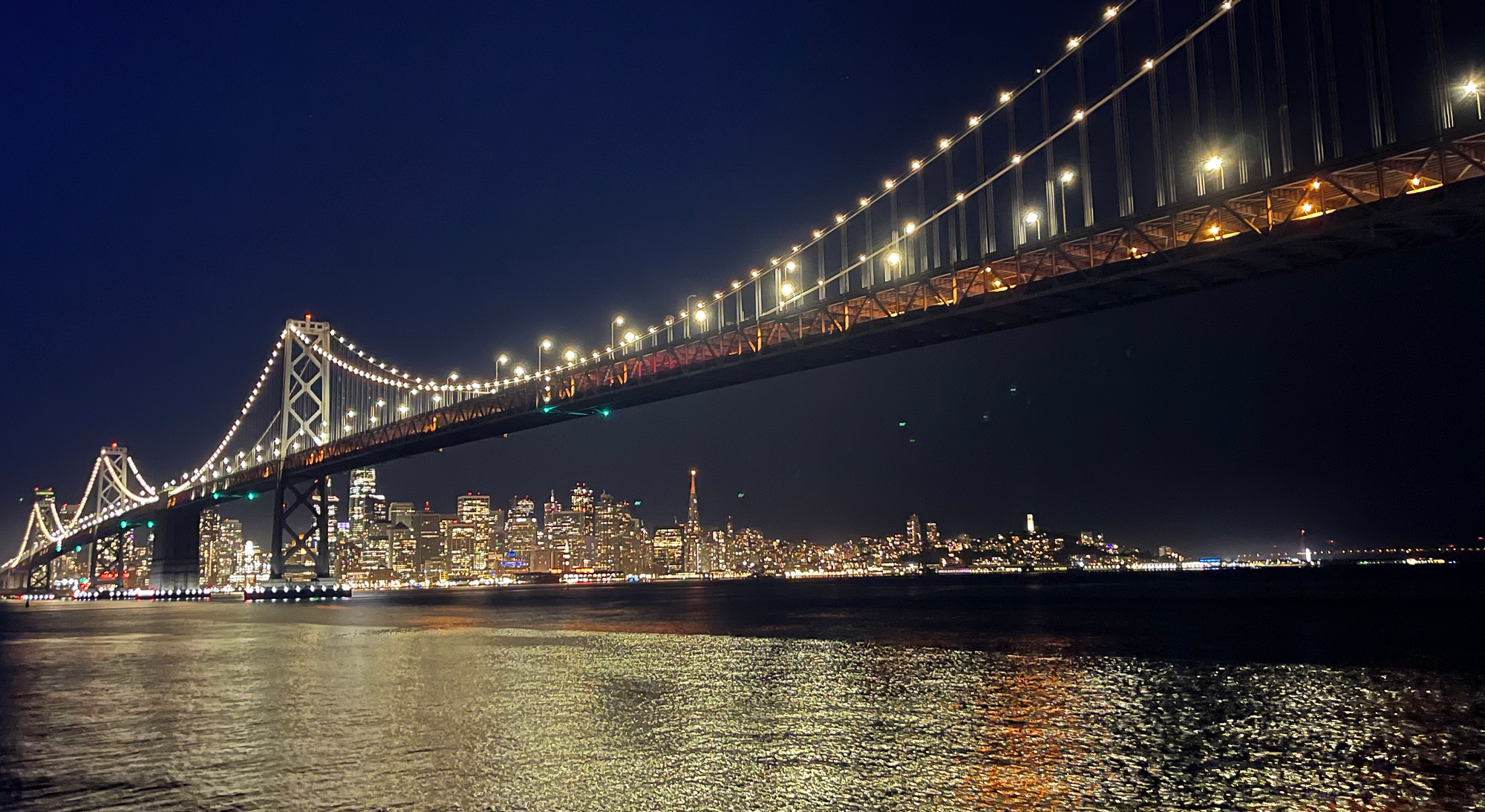 The San Francisco Bay Bridge and skyline at night from the water during FastSpring's D2Sea yacht party.