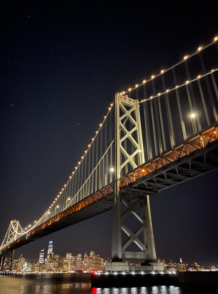The San Francisco Bay Bridge and skyline at night from the water.