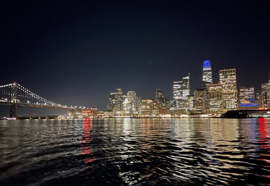 The San Francisco Bay Bridge and skyline at night from the water.