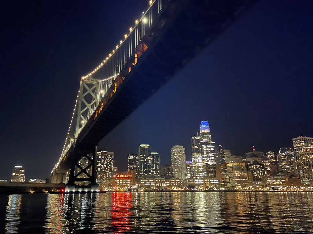 The San Francisco Bay Bridge and skyline at night from the water.